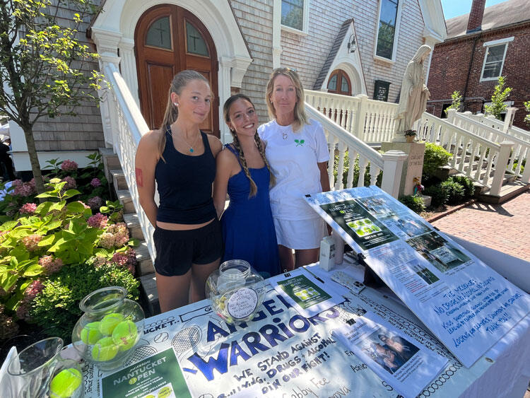 Three Angel Warriors beside an outdoor table laid out with Angel Warriors material